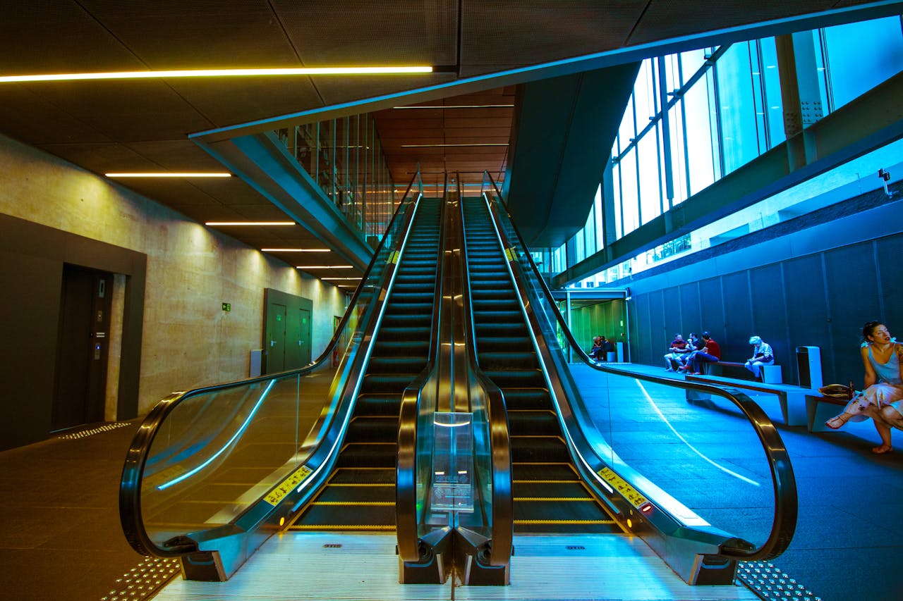 A modern indoor escalator in an urban building with sitting people. Vibrant architectural design.