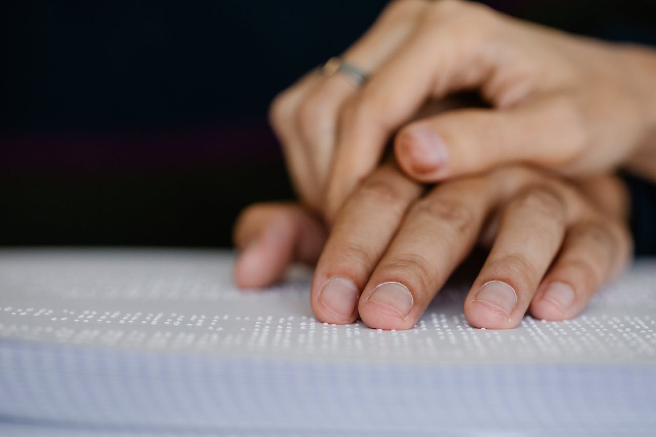 A detailed shot of hands touching a Braille book, symbolizing accessibility and visual impairment.